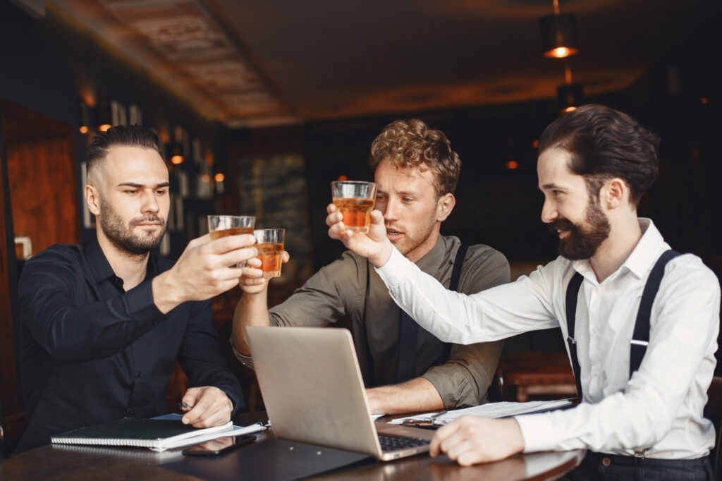 Three men raising whiskey glasses while working, celebrating, and toasting to good times.
